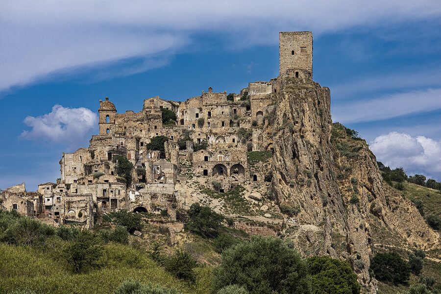 The abandoned medieval ghost town of Craco in Basilicata, empty buildings stacked on a hilltop against blue sky