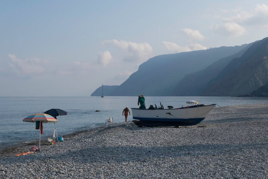A quiet Calabrian beach near Reggio with a boat docked in the foreground and green hills beyond