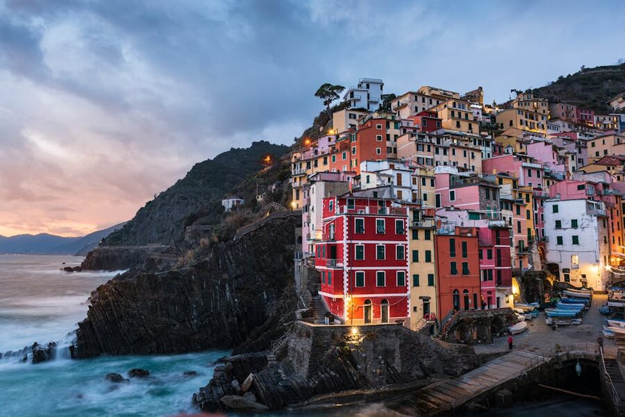 Riomaggiore village at sunset with pastel houses climbing the cliff and the small marina with fishing boats