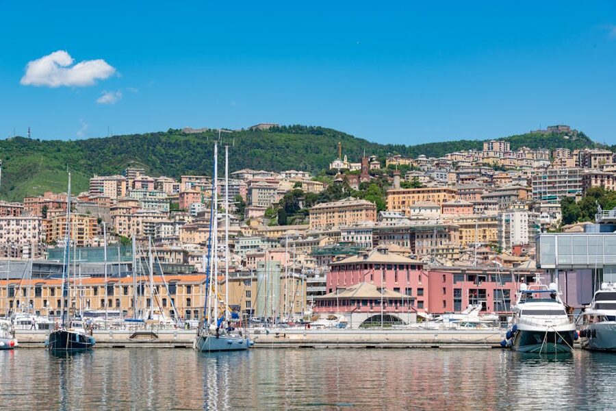 Genoa marina with sailing boats and the Ligurian hillside townscape behind in warm sunlight