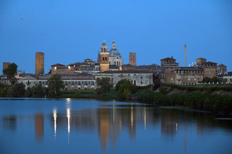 Mantova skyline at twilight reflected in the Lago di Mezzo, with the Ducal Palace and historic towers