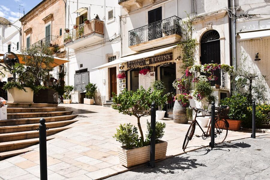 A sunny whitewashed street in Ostuni, Puglia, with a bicycle and flowers