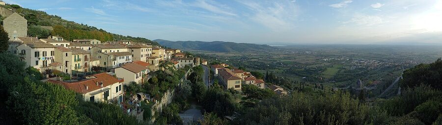 The hilltop town of Cortona in Tuscany with terracotta roofs and the Val di Chiana below