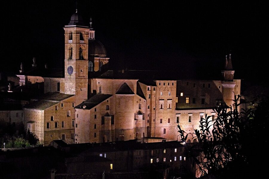 The Palazzo Ducale in Urbino illuminated at night with reflections on the cobbled square